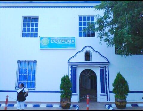 White building with blue-trimmed windows and a COOPEMA sign above the entrance