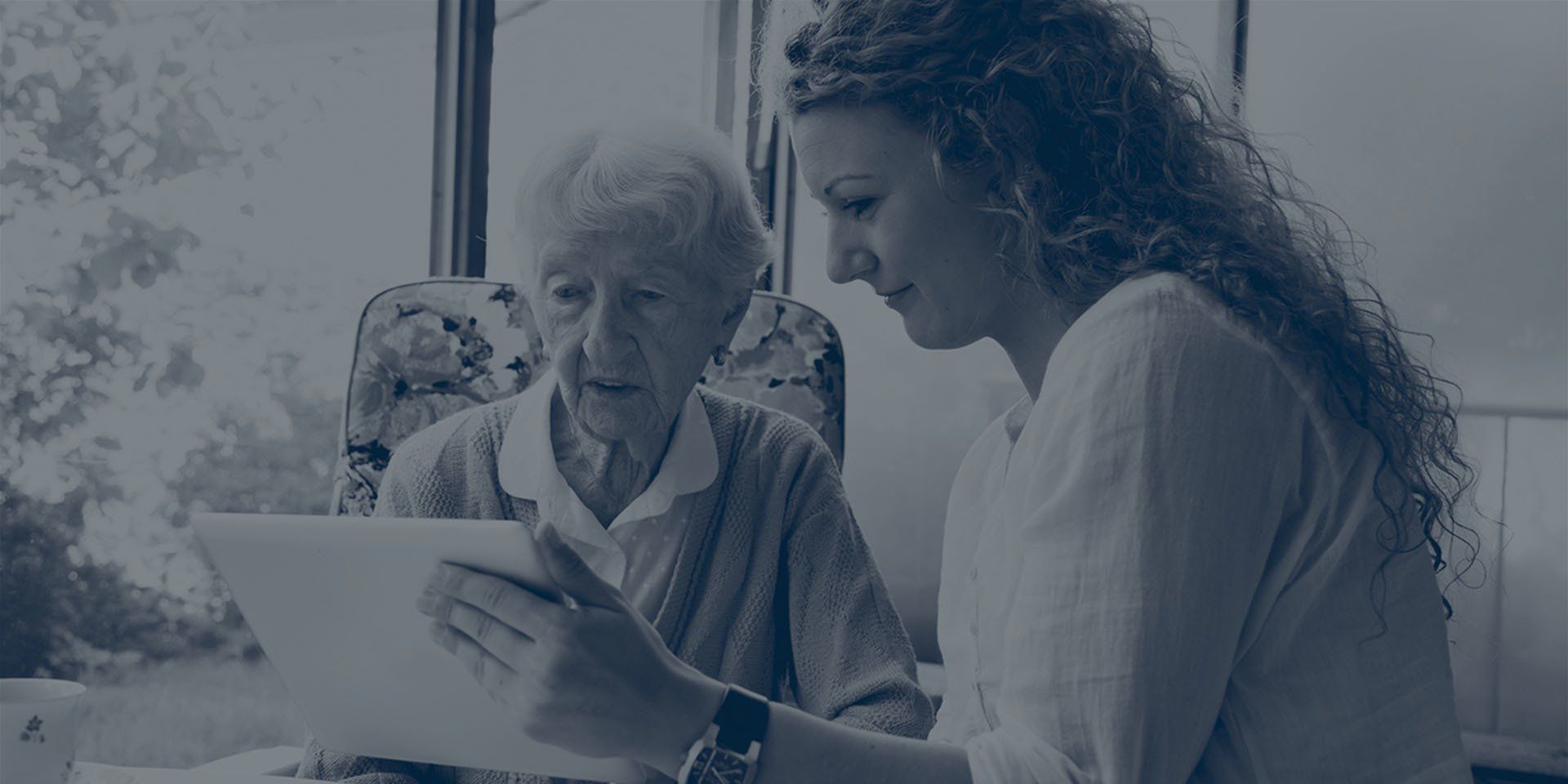A woman is teaching an elderly woman how to use a tablet computer.