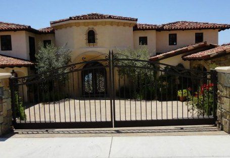 A large beige house with a red tile roof and wrought iron gate.