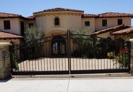 Large house with wrought iron gate; beige stucco walls, red tile roof, arched entryway.