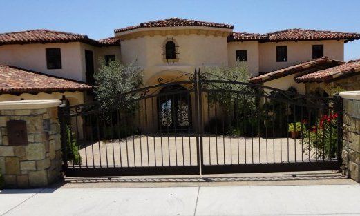 Large beige house with tile roof, gated driveway.