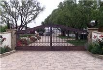 Brown wrought iron driveway gate with brick paving and landscaping.