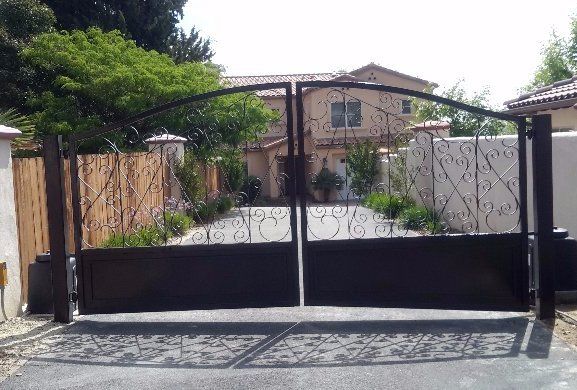 Black wrought iron driveway gates with a house in the background.