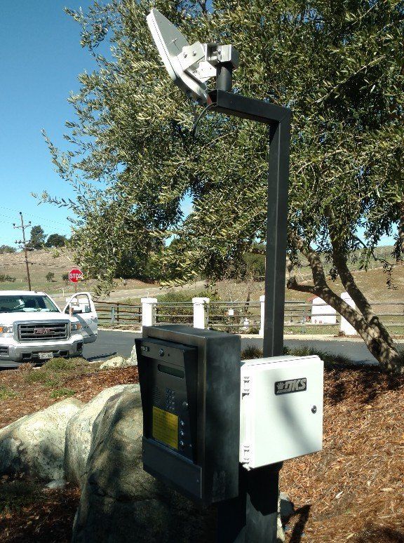 Outdoor equipment for communication and access control, with a white vehicle and trees in the background.
