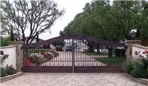 Ornate, wrought-iron driveway gate, brick pillars, and landscaped yard.