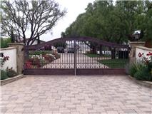 Brown metal driveway gate with brick columns and a paved entrance.