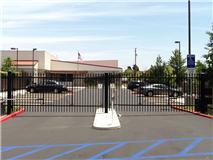 Black metal gate at the entrance of a building with cars behind it; blue sky above.