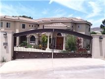 Brown iron gate in front of a large, two-story beige house with a tiled roof. Sunny day.