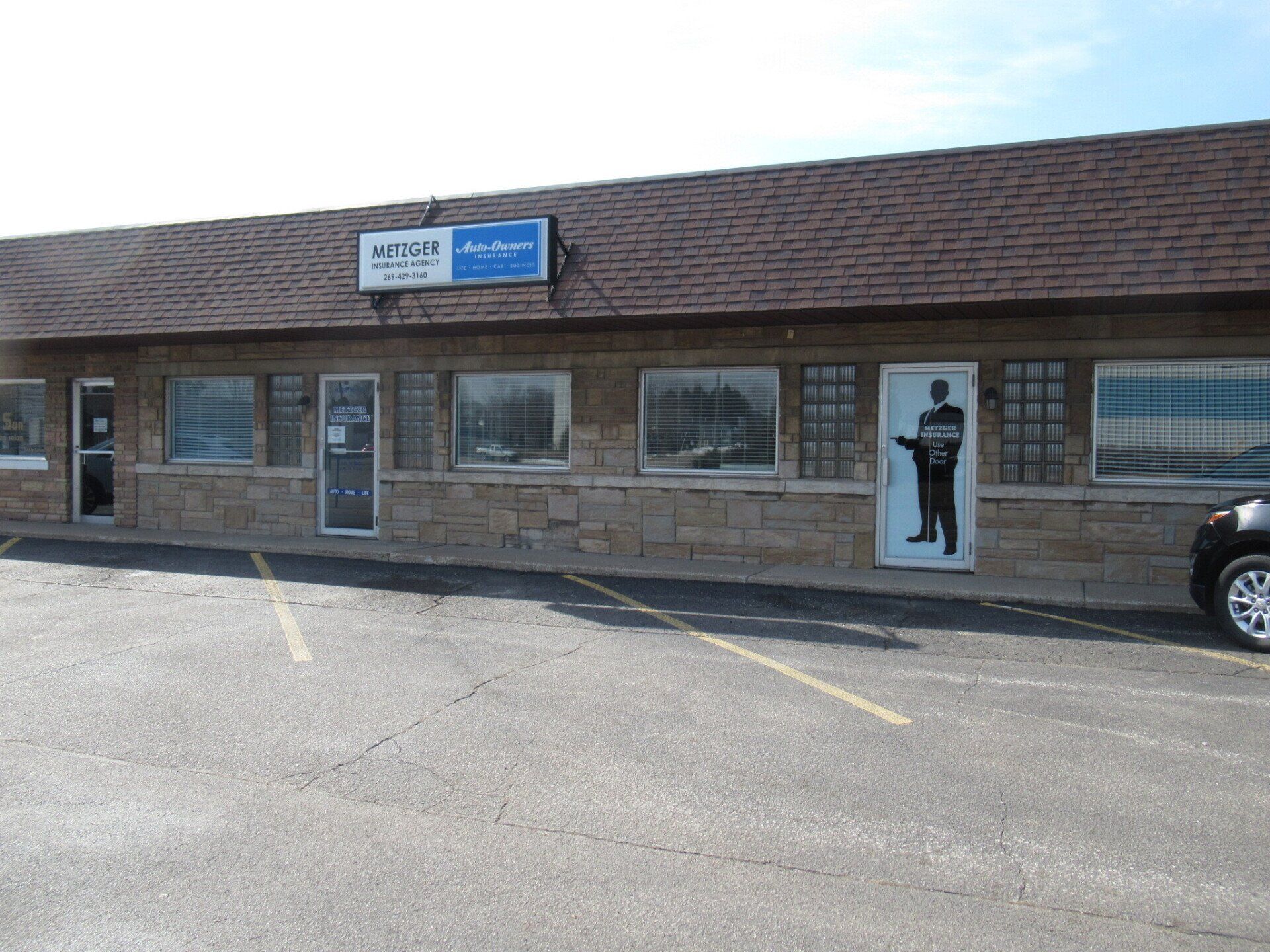 Exterior of a brick building with several windows, a sign, and a black-and-white door with a silhouette.