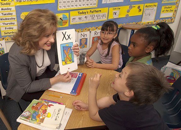 Image of a teacher holding a letter card for three students