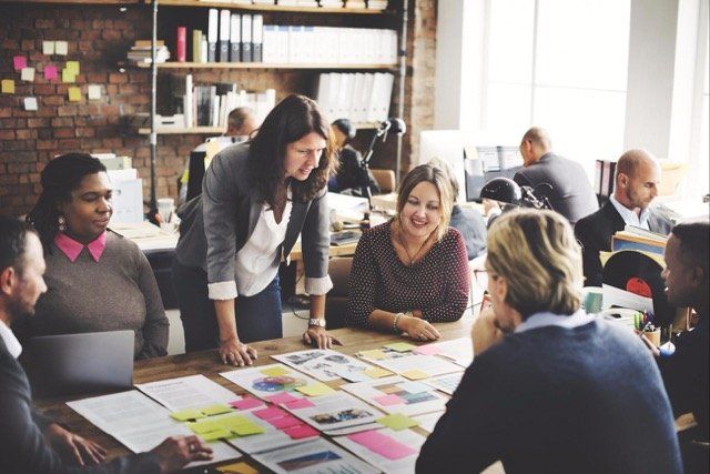 Image shows a table of six male and female educators sitting around a set of papers that are labeled with sticky notes