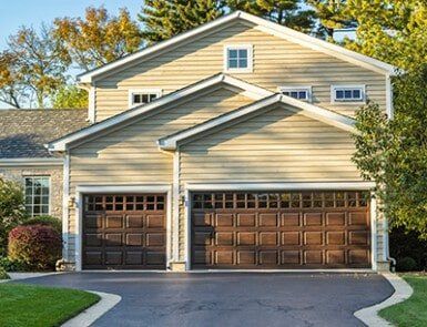 Suburban beige house with three-car garage and paved driveway, framed by trees and greenery