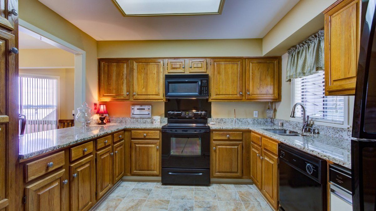 A kitchen with wooden cabinets , black appliances and granite counter tops.