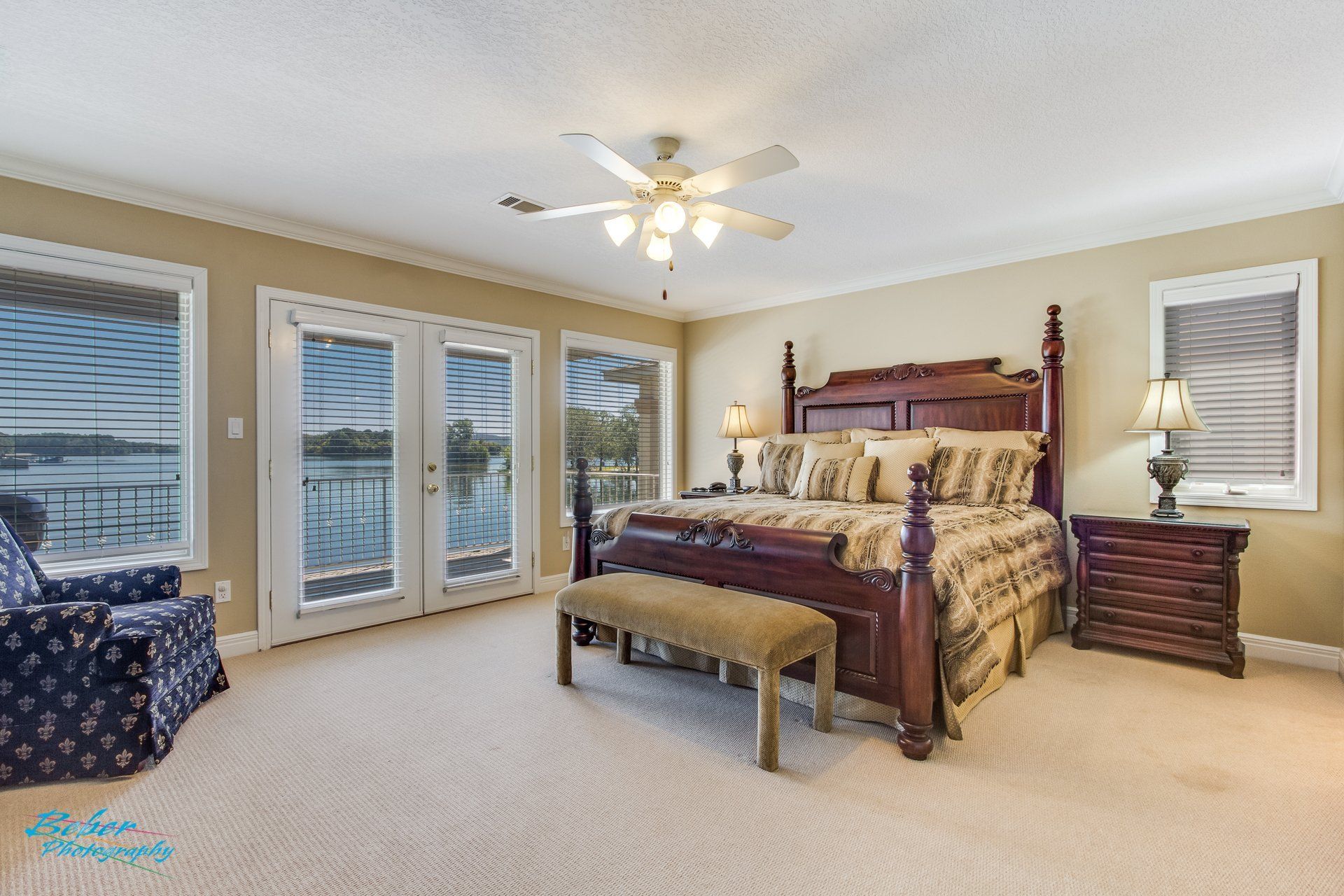 A bedroom with a king size bed , chair , nightstand and ceiling fan.