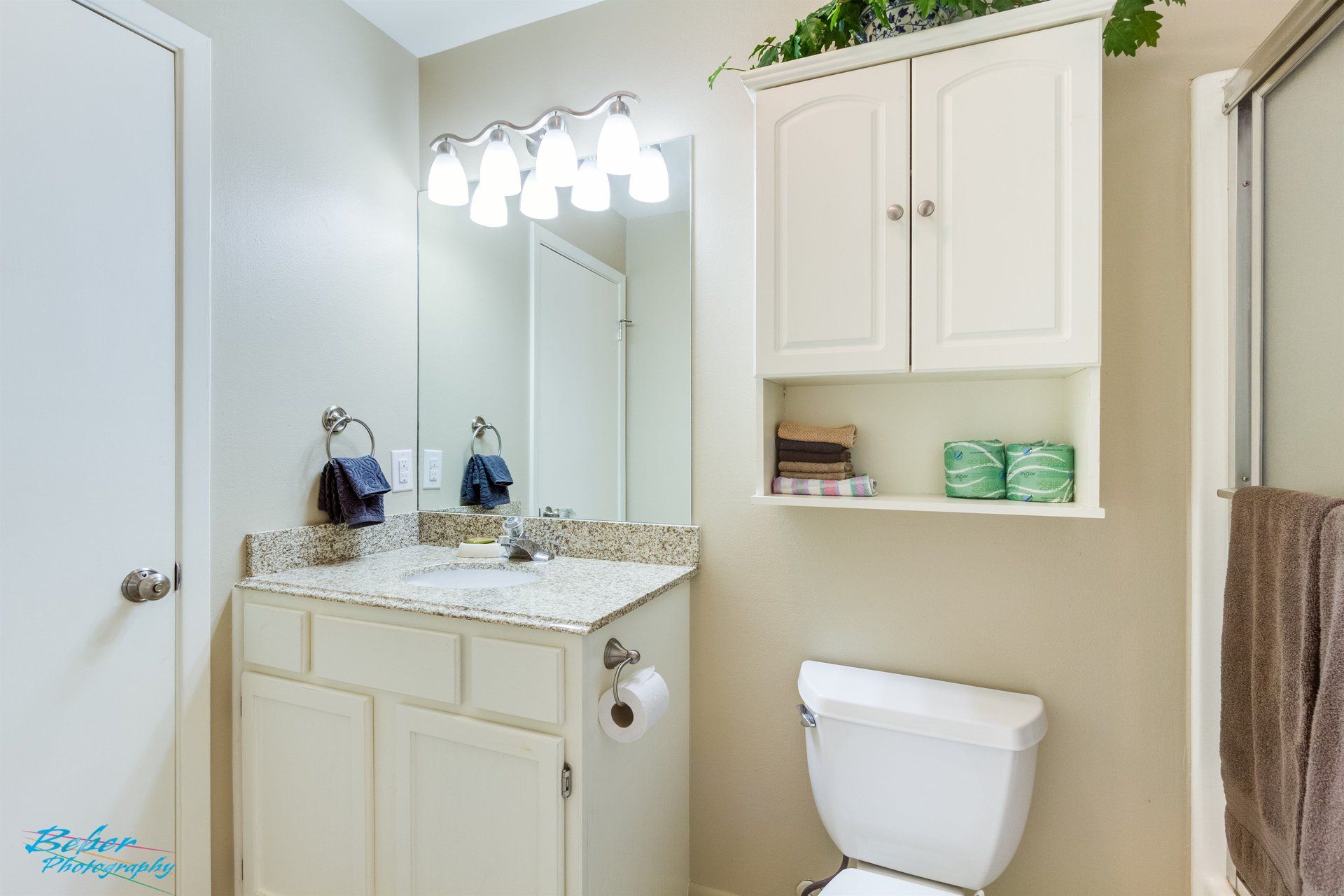 A bathroom with a toilet , sink , mirror and cabinets.