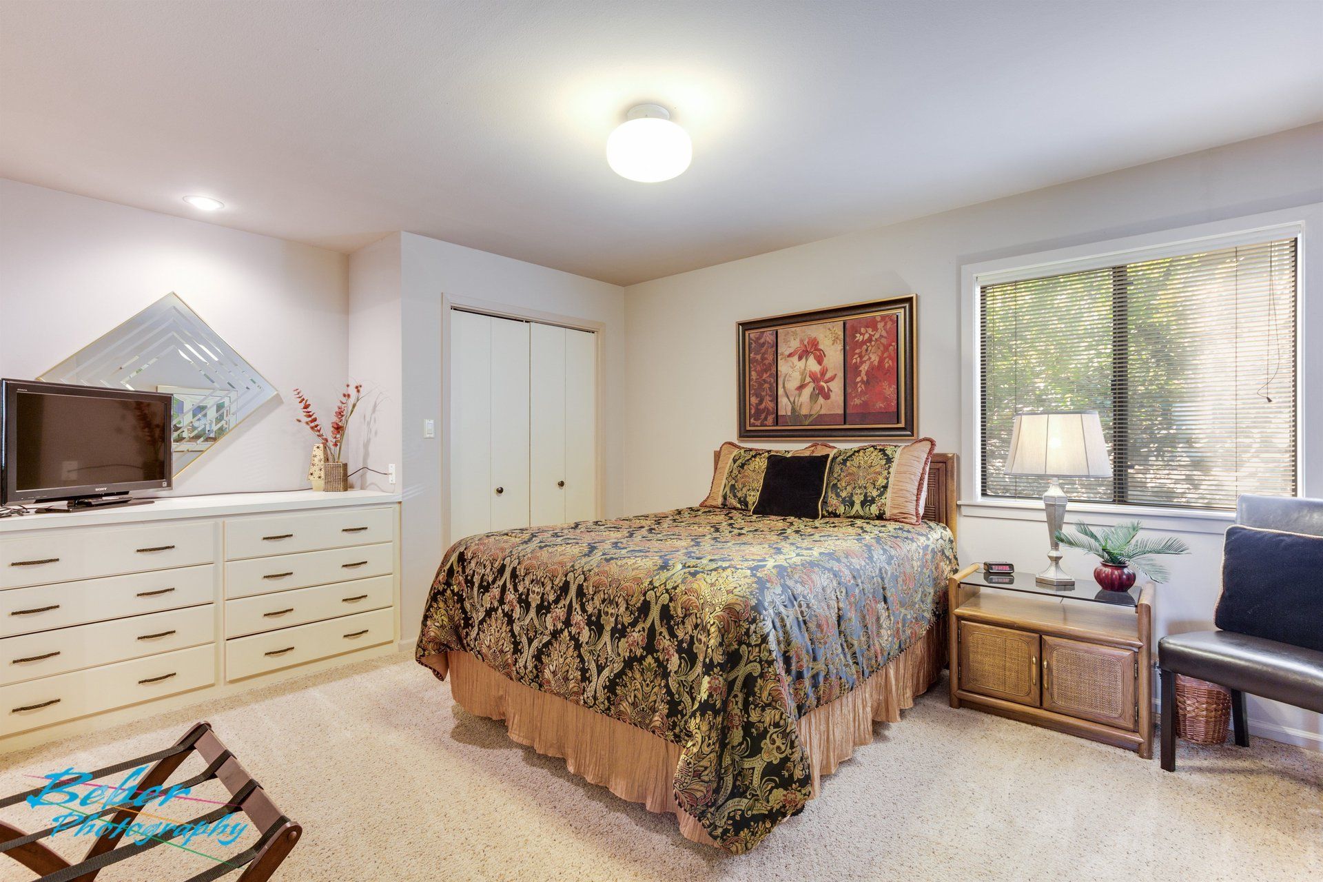 A bedroom with a large bed , dresser , chair and television.