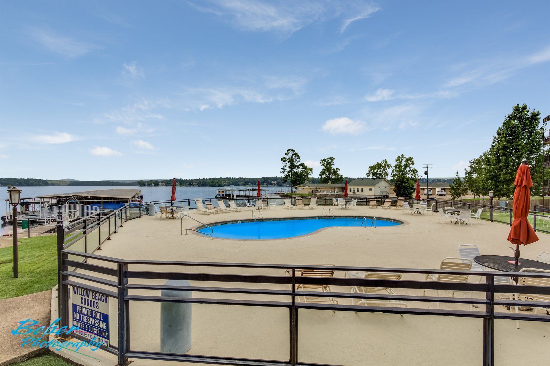 A large swimming pool surrounded by chairs and umbrellas next to a lake.