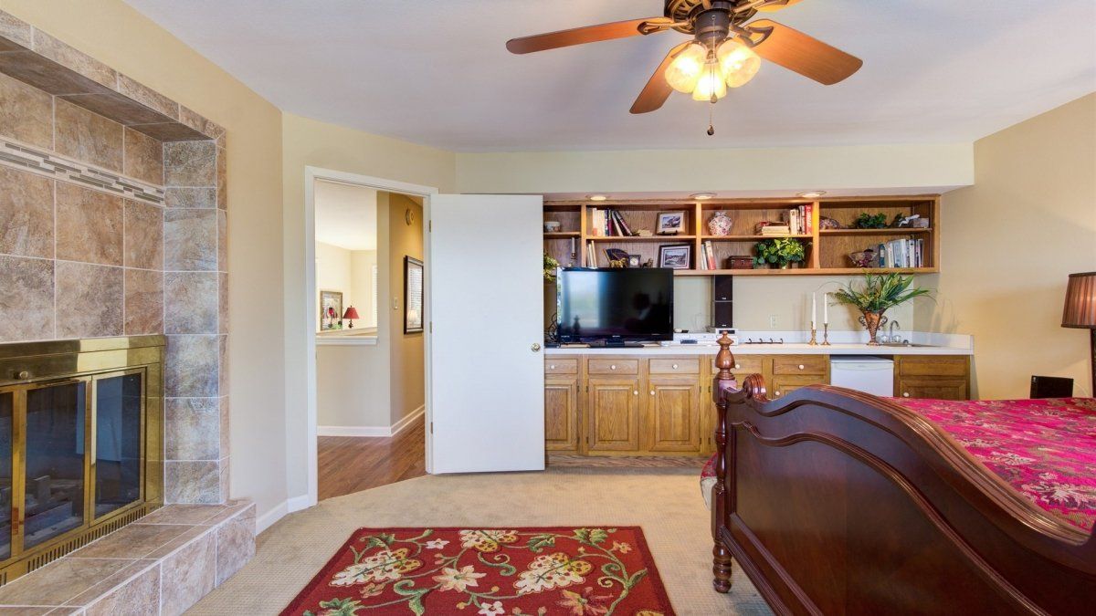 A bedroom with a bed , fireplace , television and ceiling fan.
