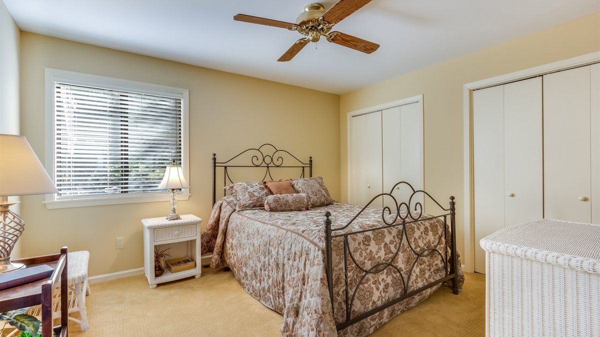 A bedroom with a bed , nightstand , lamp and ceiling fan.