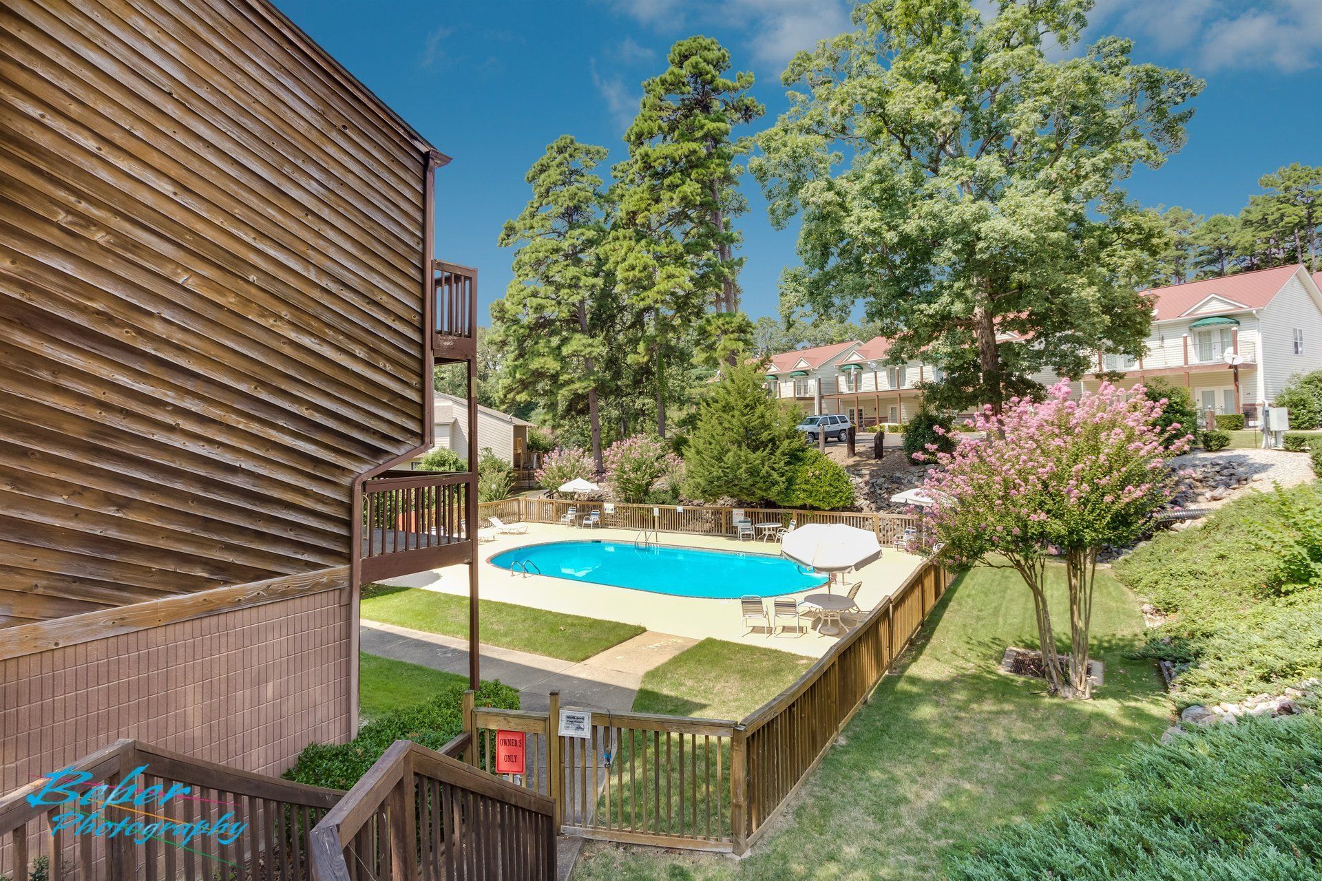 A large swimming pool is surrounded by a wooden fence in a residential area.