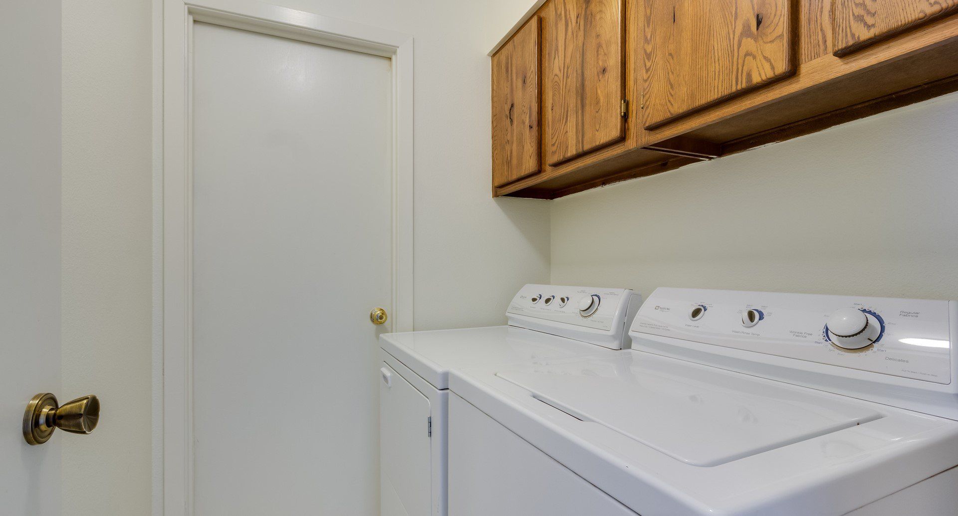 A laundry room with a washer and dryer and wooden cabinets.