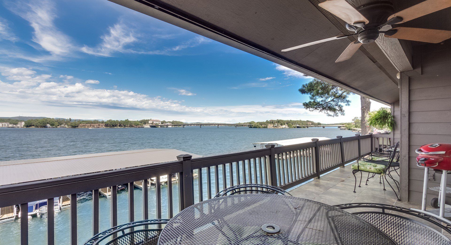 A balcony overlooking a lake with a table and chairs and a ceiling fan.