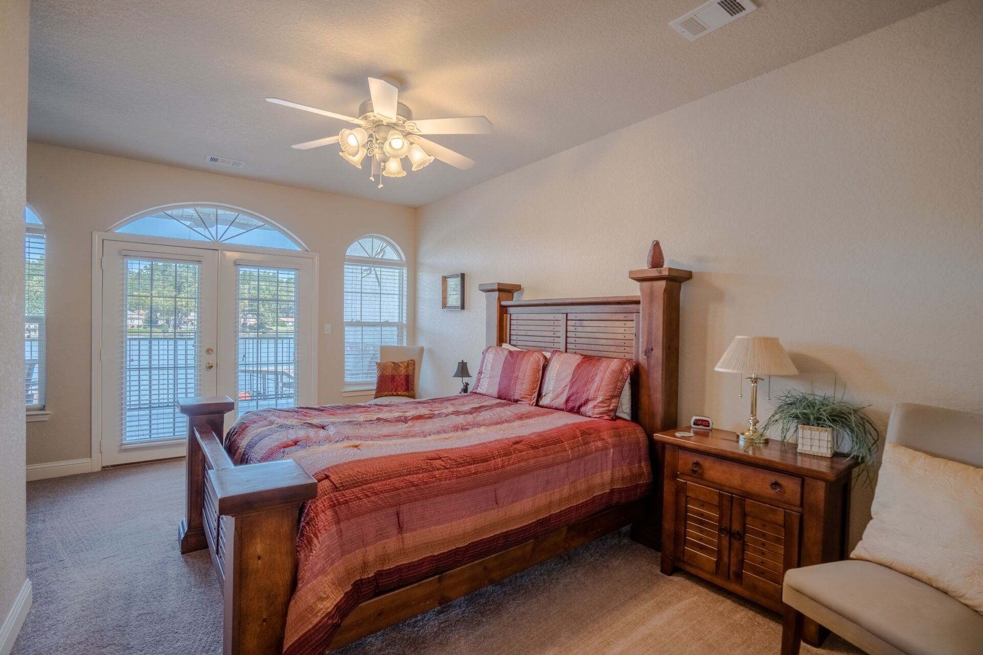 A bedroom with a large bed , nightstand , chair and ceiling fan.
