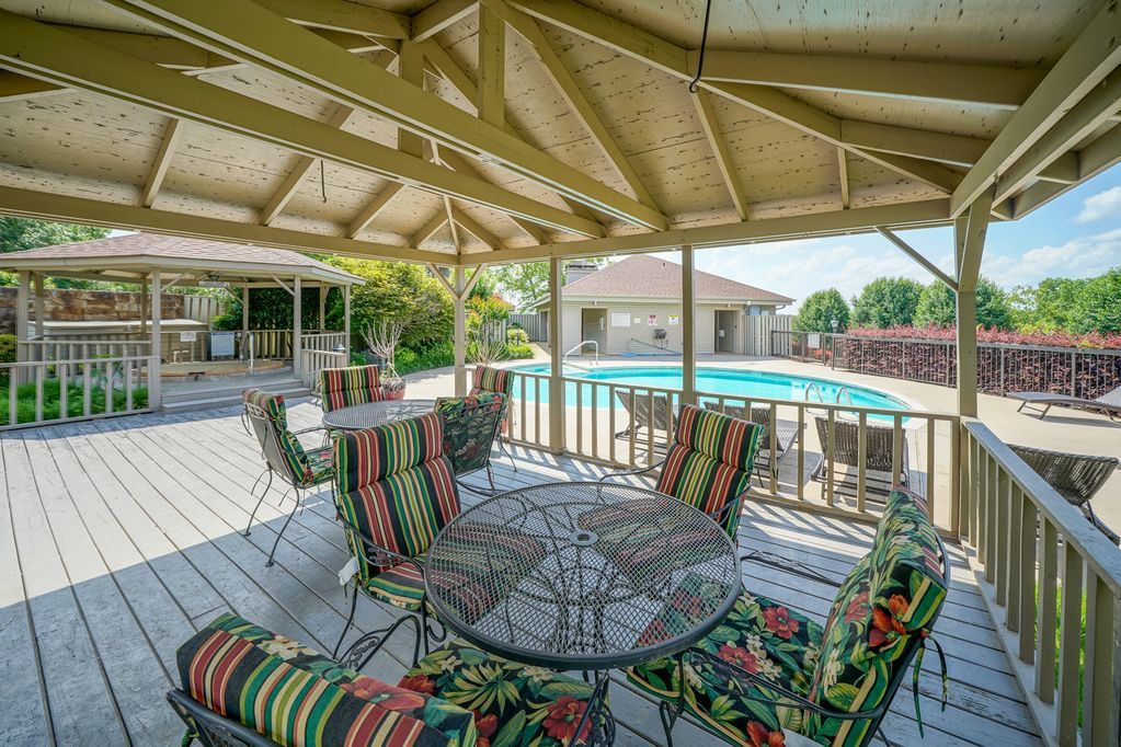 A patio with a table and chairs under a canopy overlooking a pool.