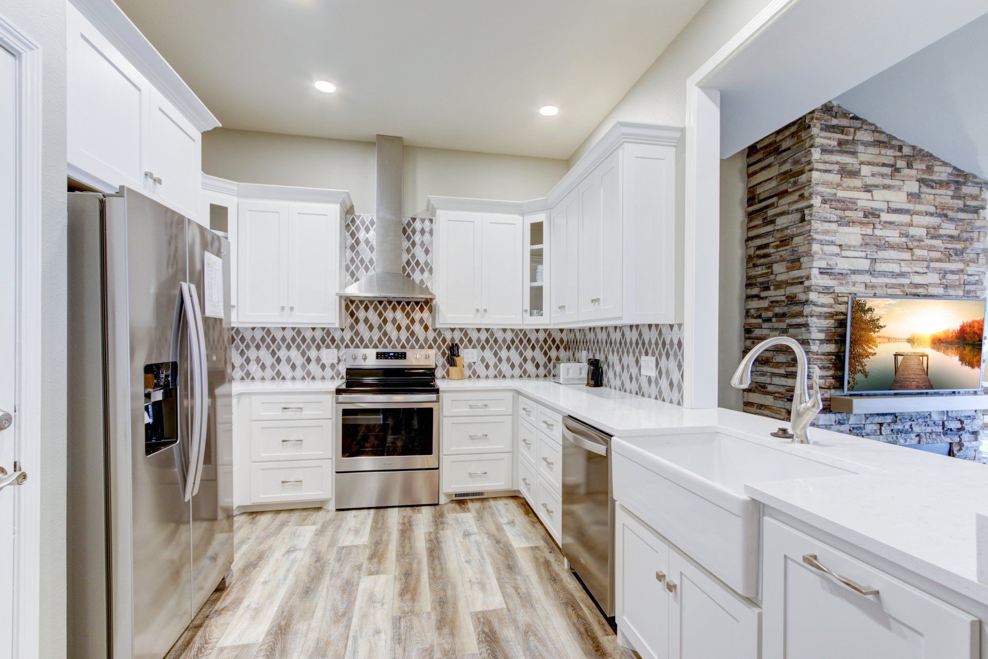 A kitchen with white cabinets , stainless steel appliances , a sink and a refrigerator.