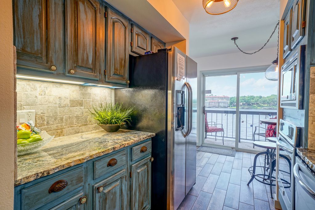 A kitchen with blue cabinets , granite counter tops , stainless steel appliances and a sliding glass door.
