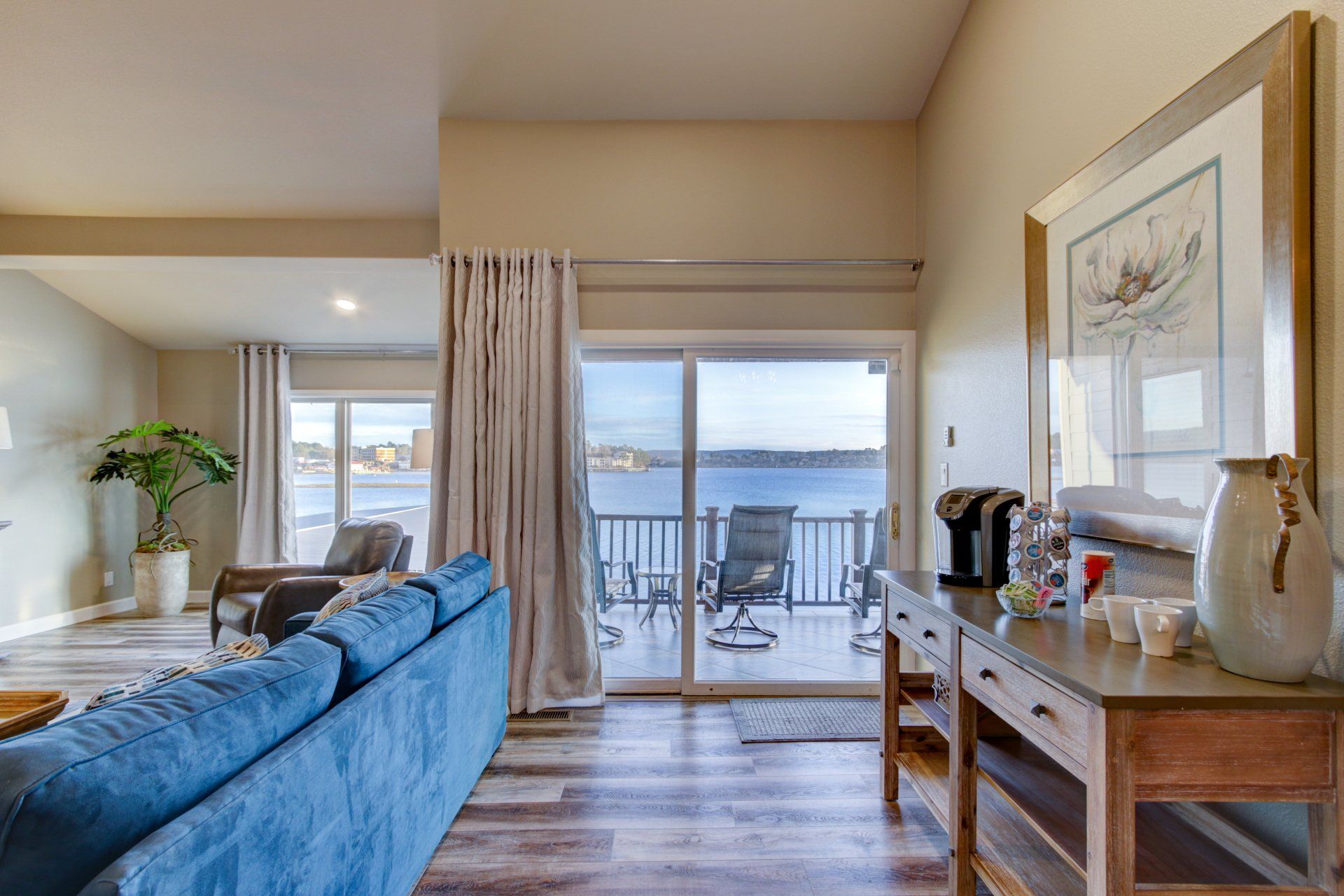 A living room with a blue couch and a sliding glass door leading to a balcony overlooking the water.