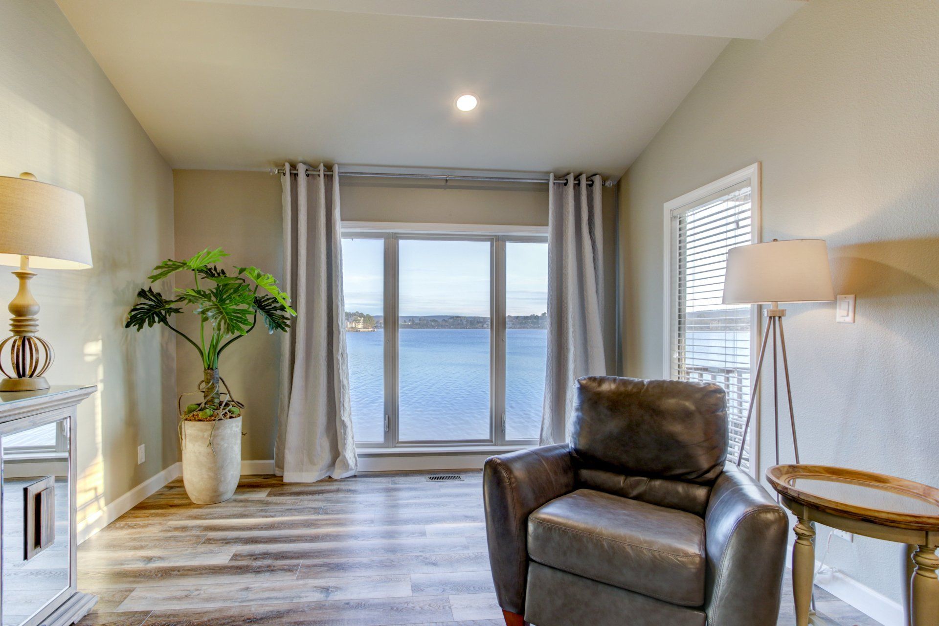 A living room with a chair , table , lamps and a large window overlooking the water.