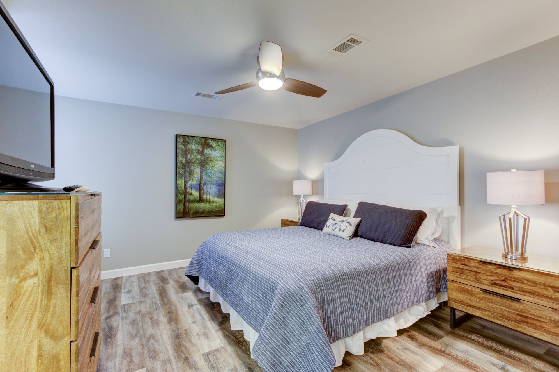 A bedroom with a king size bed , dresser , nightstand , television and ceiling fan.