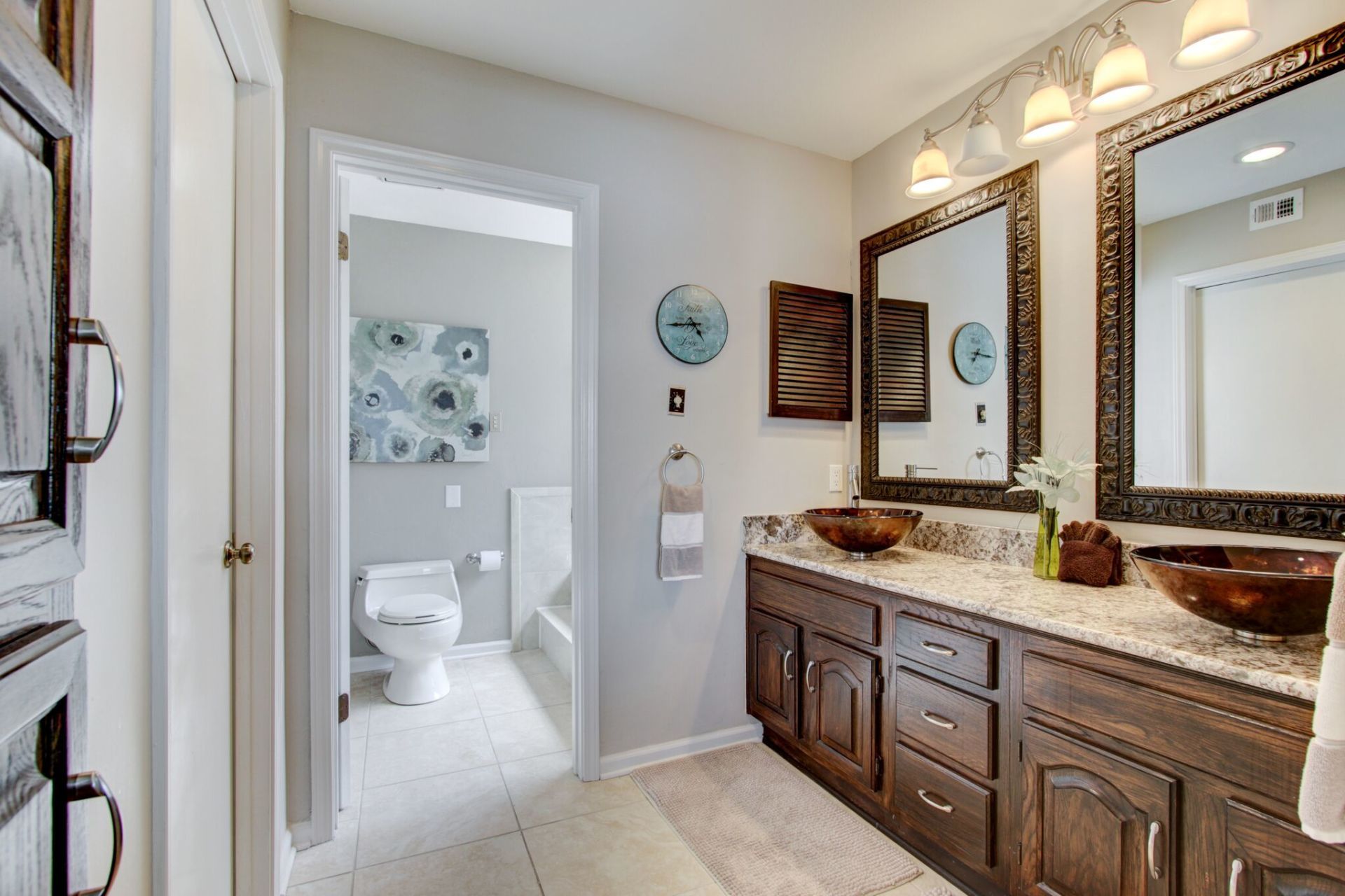 A bathroom with two sinks , two mirrors and a toilet.