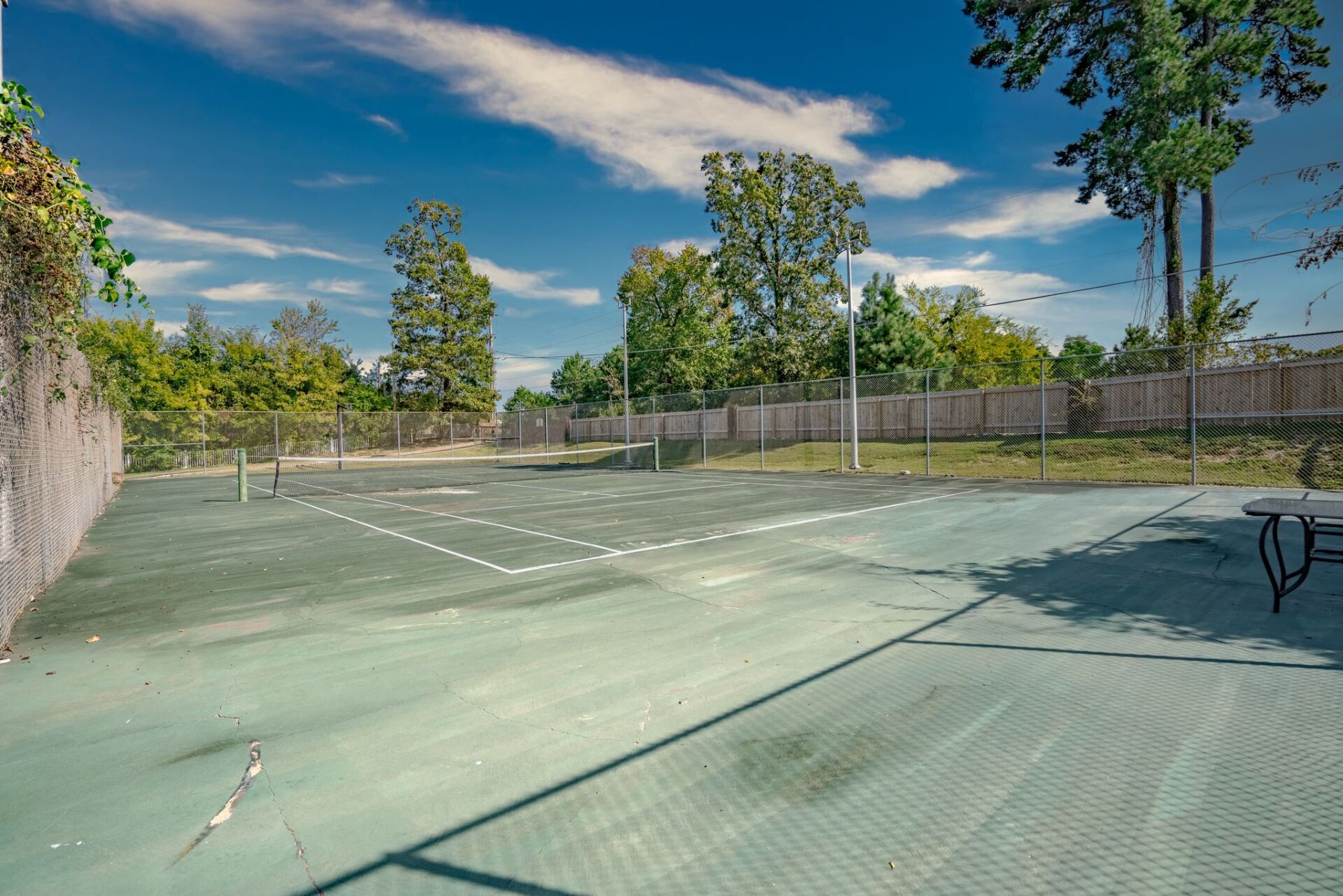 An empty tennis court with a fence and trees in the background