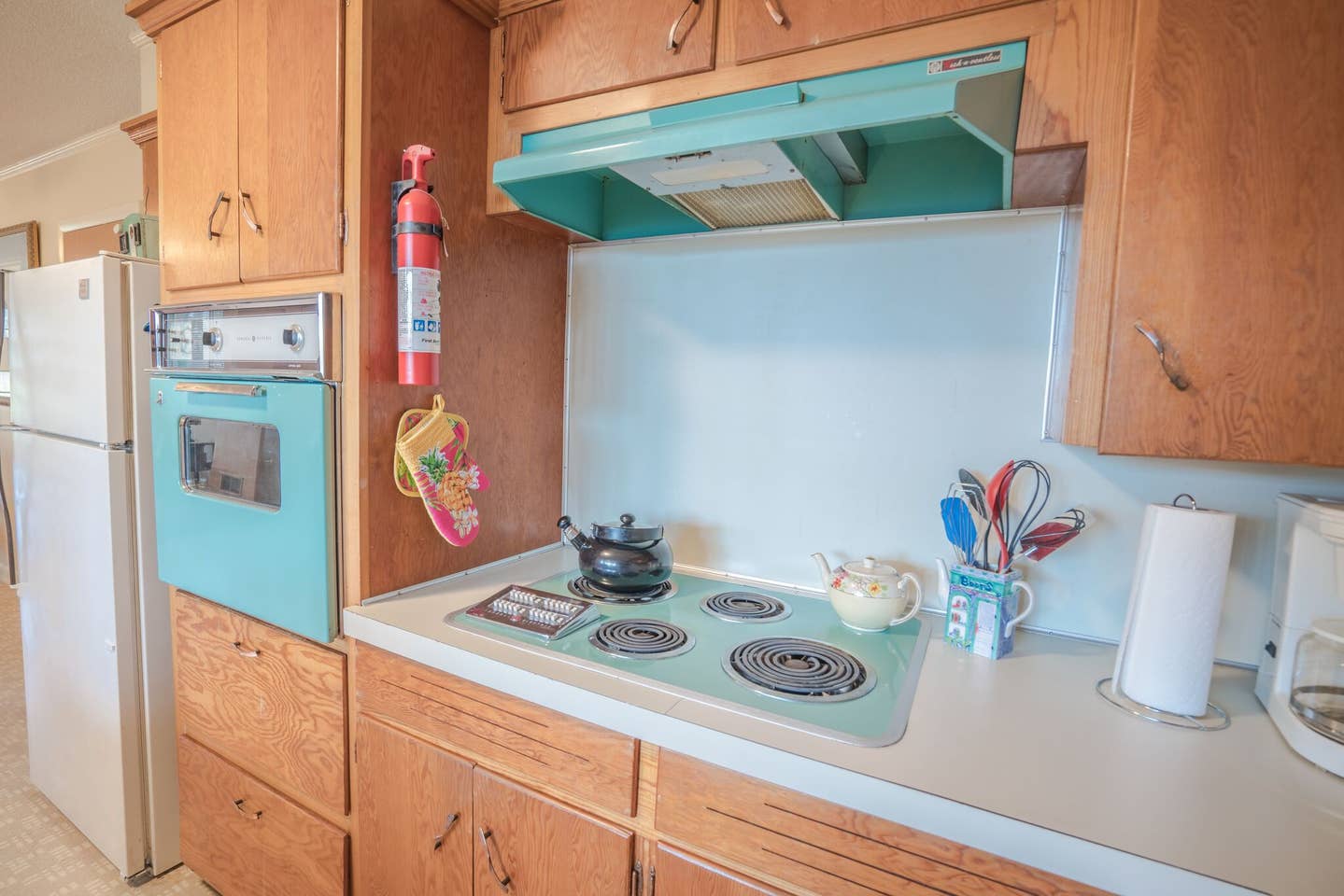 A kitchen with wooden cabinets , a blue stove top oven , and a white refrigerator.