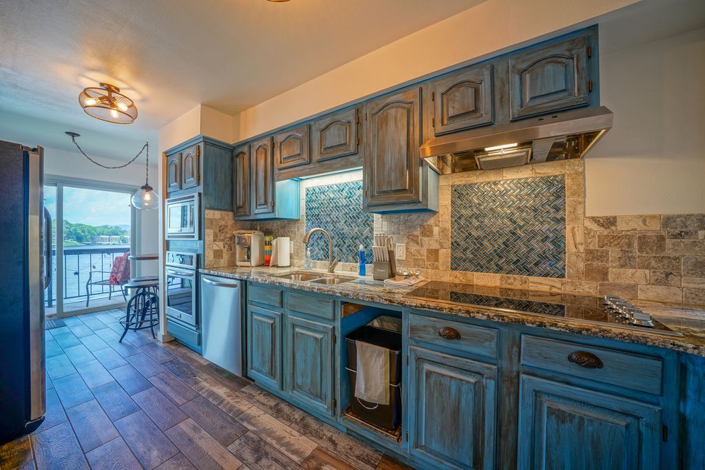 A kitchen with blue cabinets , granite counter tops , and stainless steel appliances.