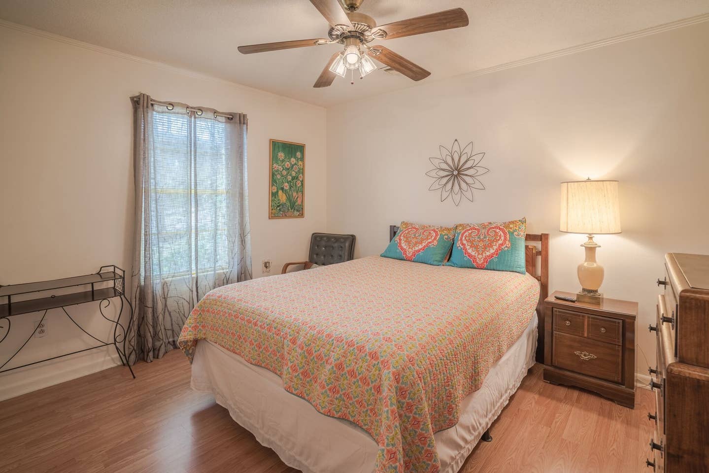 A bedroom with a bed , nightstand , dresser and ceiling fan.