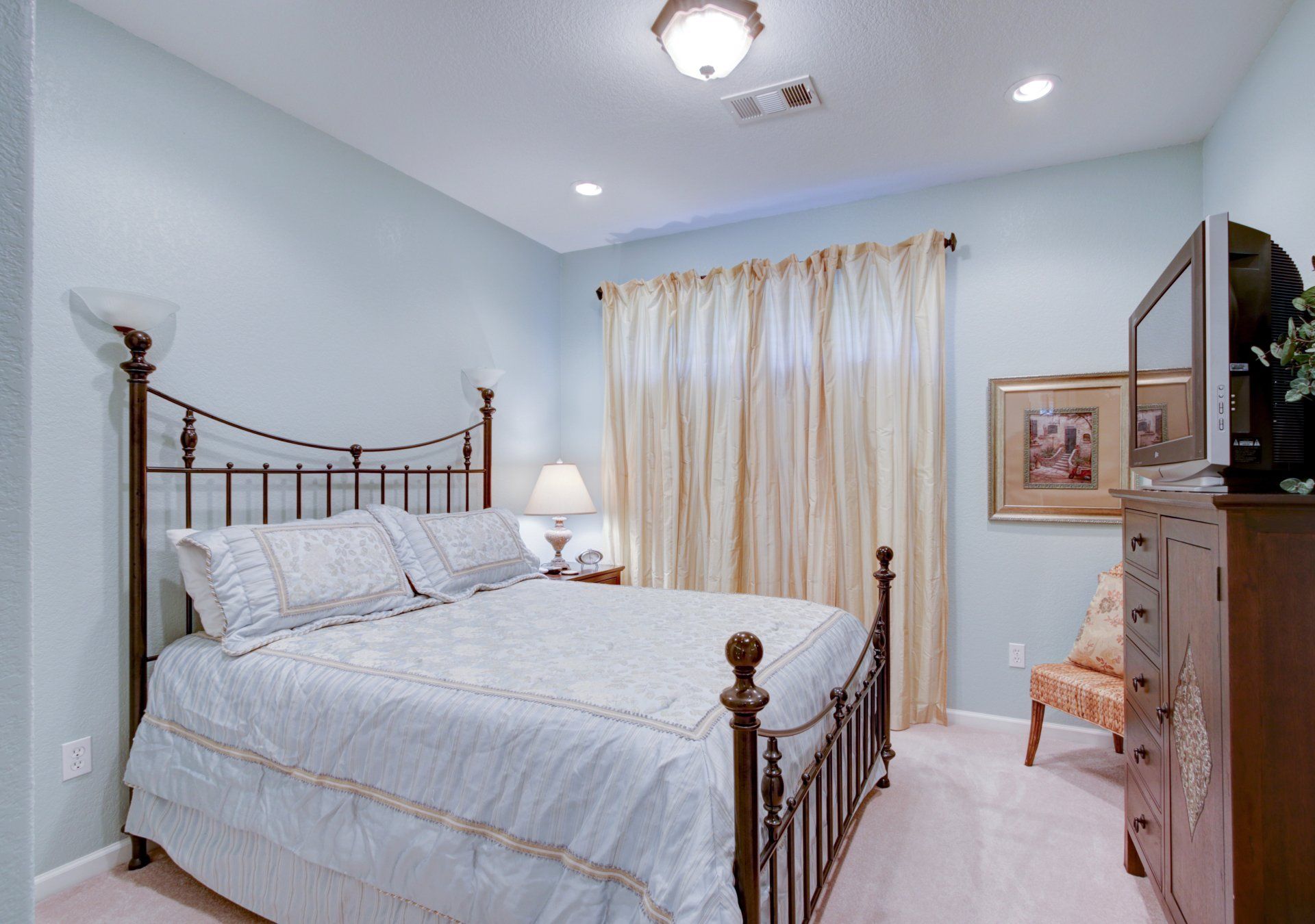 A bedroom with a king size bed , dresser , chair and television.