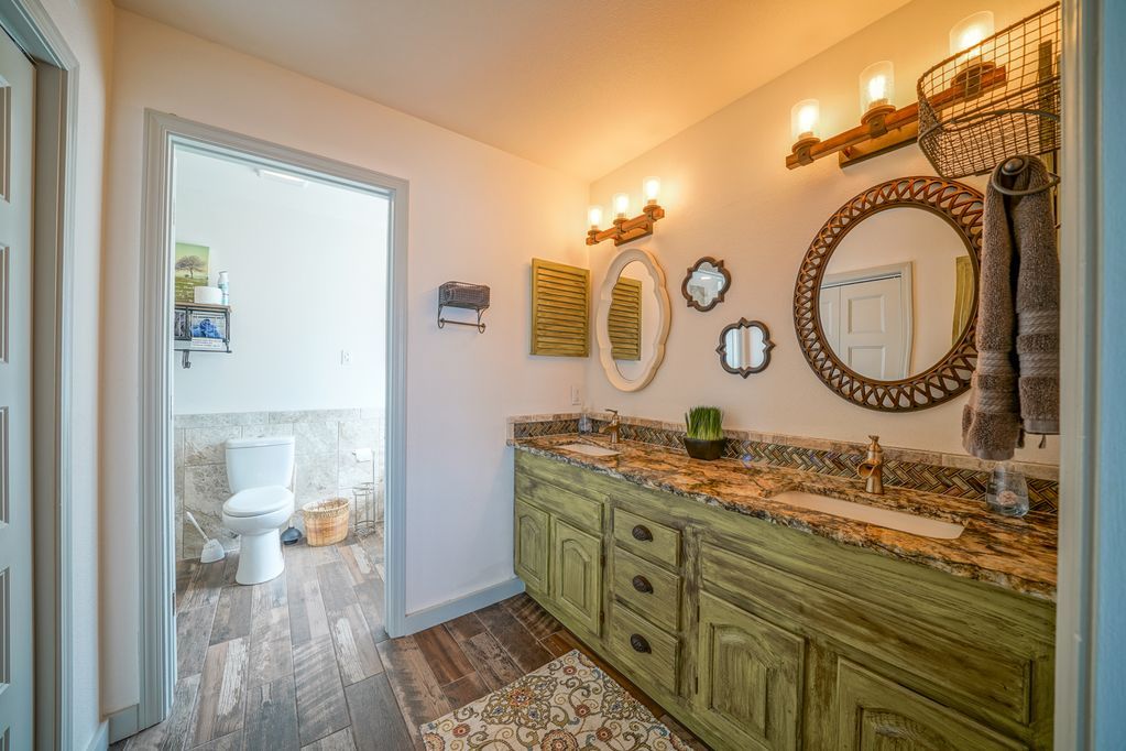 A bathroom with green cabinets , granite counter tops , mirrors and a toilet.