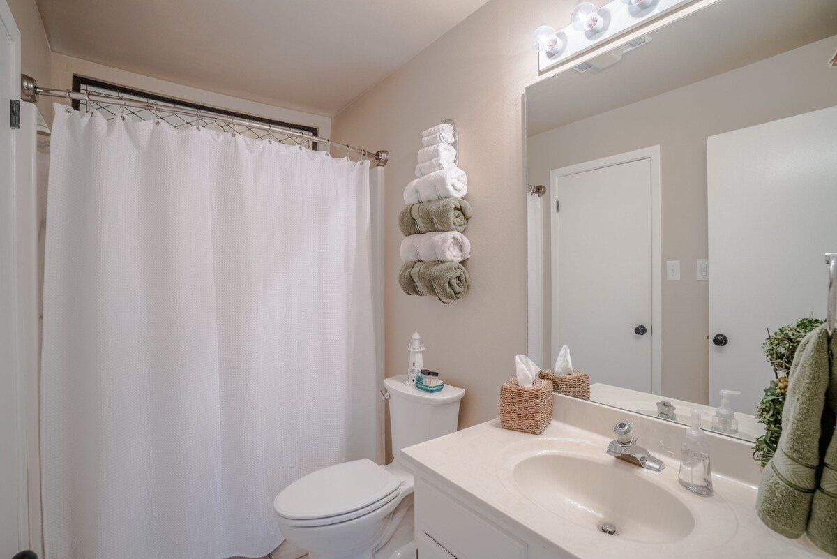 A bathroom with a toilet , sink , mirror and shower curtain.