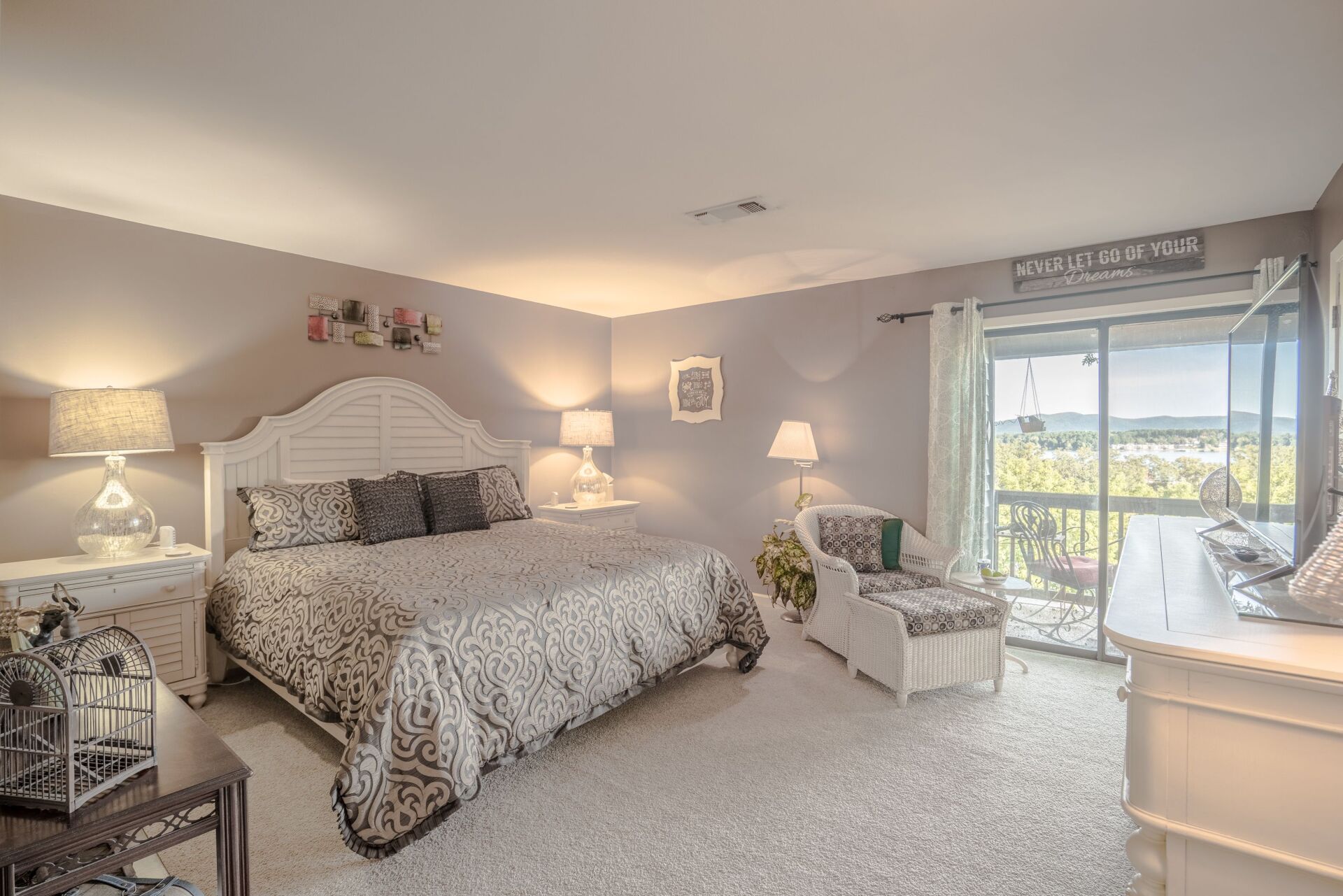 A bedroom with a king size bed , dresser , chair and sliding glass doors.