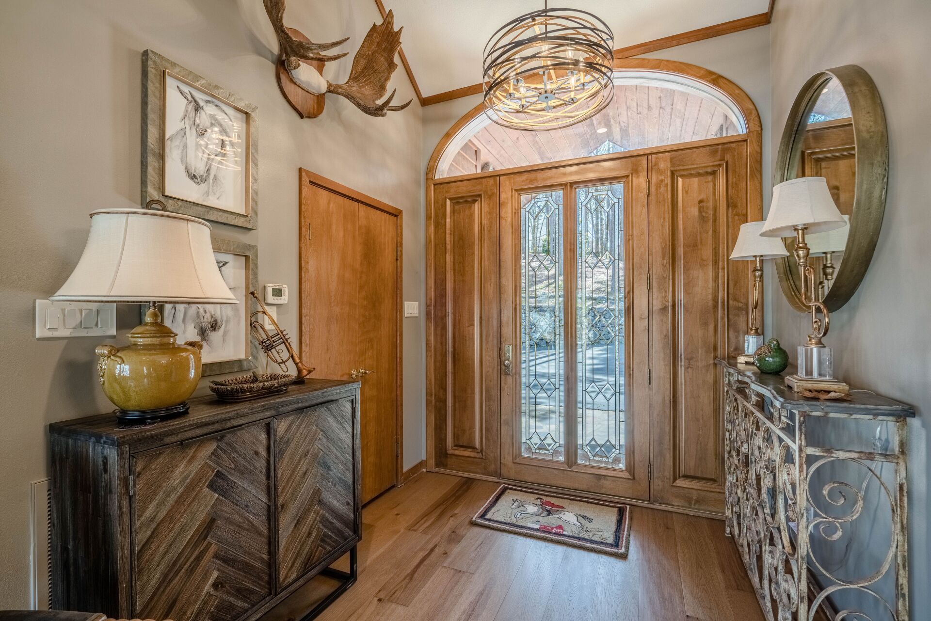 A hallway with hardwood floors , a dresser , lamps and a mirror.