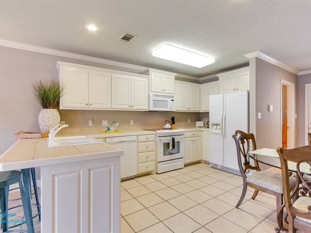 A kitchen with white cabinets , a refrigerator , a microwave , a sink , and a table.