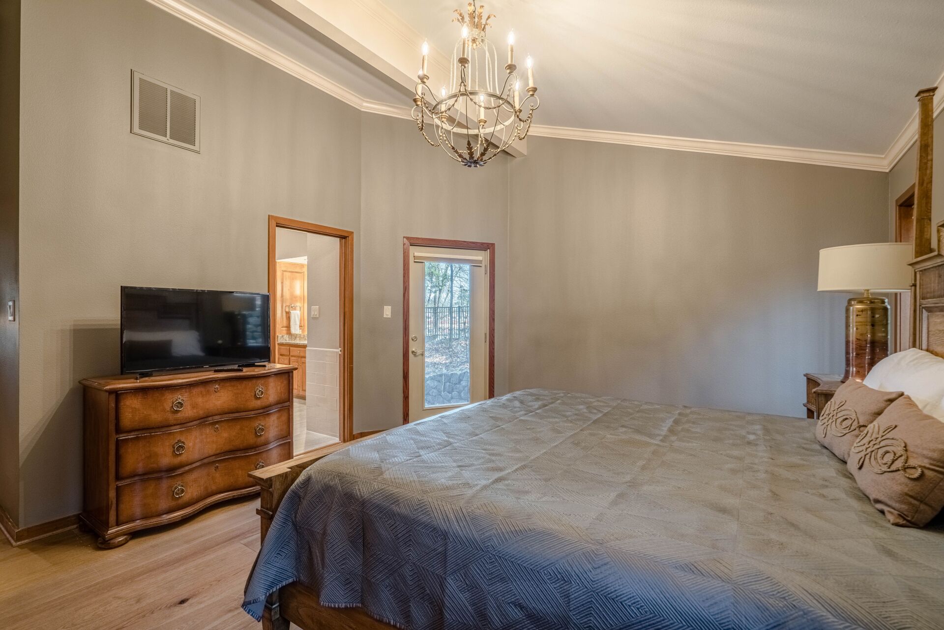A bedroom with a bed , dresser , television and chandelier.
