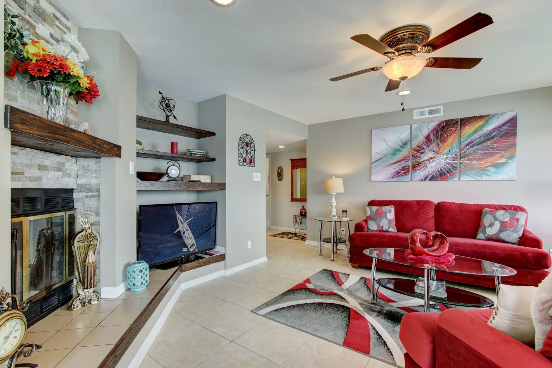 A living room with a red couch , fireplace , and ceiling fan.