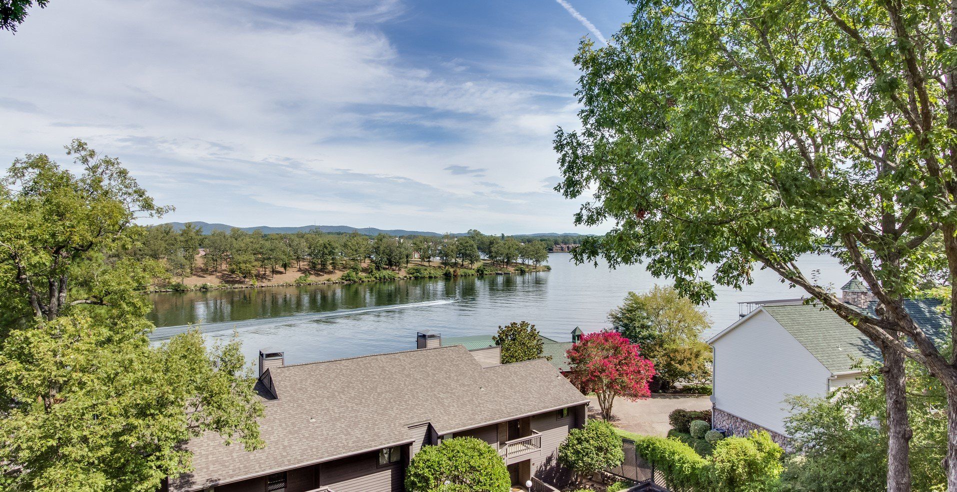 A house with a lake in the background and trees in the foreground.