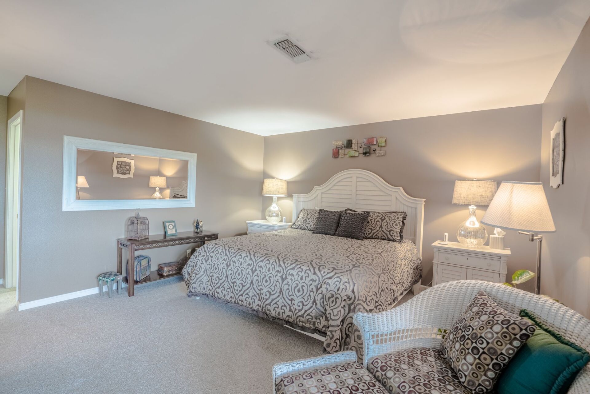 A bedroom with a large bed , chair , nightstand and mirror.