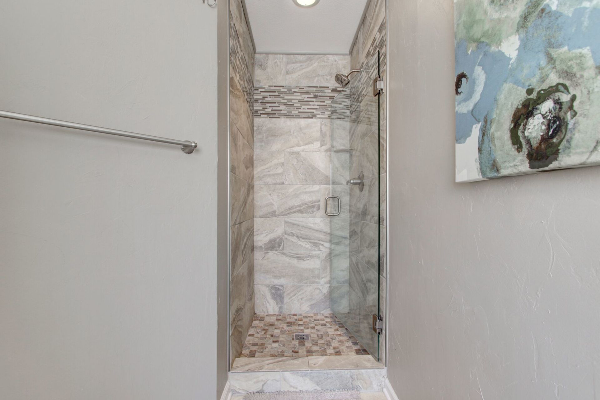 A bathroom with a walk in shower and a painting on the wall.