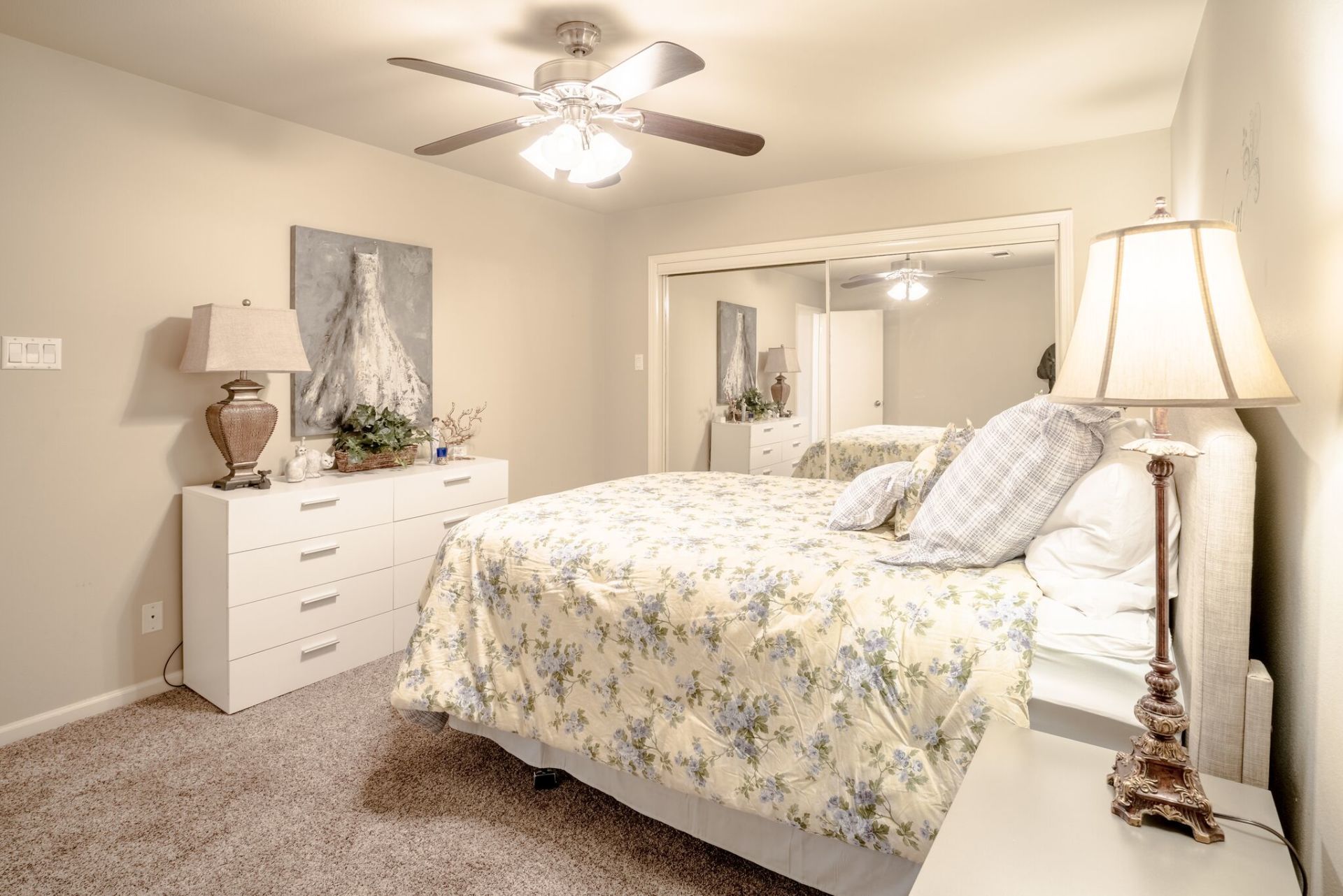 A bedroom with a bed , dresser , lamp , mirror and ceiling fan.